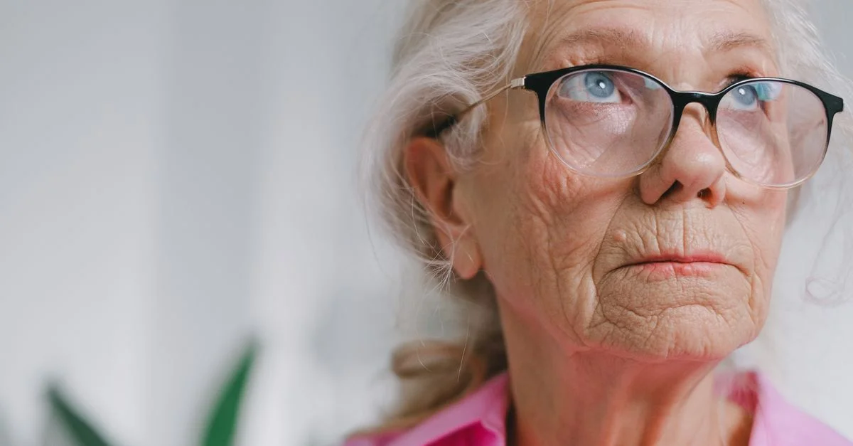 Portrait en gros plan d'une femme âgée pensive portant des lunettes à l'intérieur.